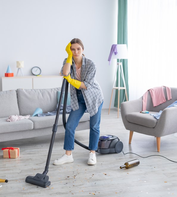 Unhappy,Young,Woman,Standing,With,Vacuum,Cleaner,In,Messy,Flat